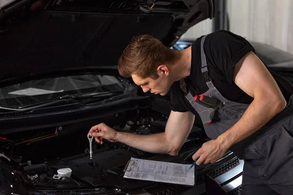 Guapo caucásico chico está tomando notas mientras la reparación de capucha de coche — Foto de Stock