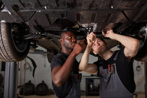Dois inter-raciais mecânica diversificada verificando fundo do carro — Fotografia de Stock