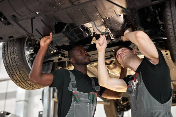 Twee interraciale diverse mechanica controleren auto onderaan — Stockfoto