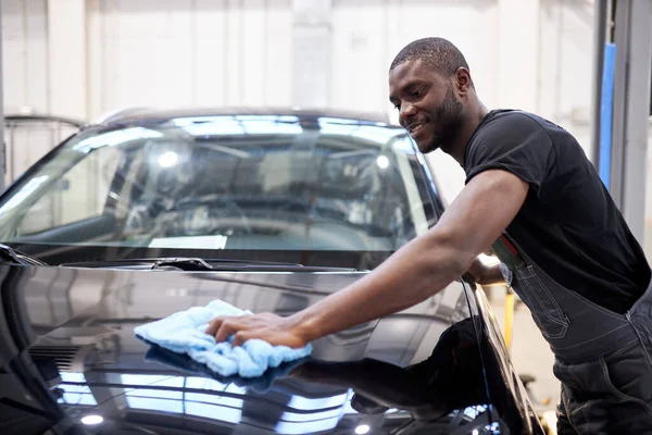Афро-американский автомеханик вытирает поверхность машины после полировки — стоковое фото