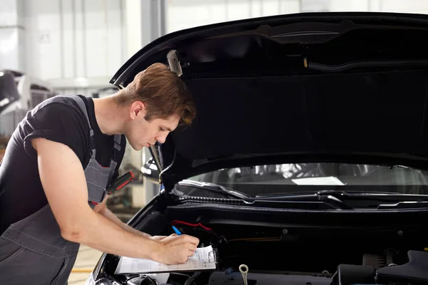 Knappe blanke man is het maken van notities tijdens het repareren van kap van de auto — Stockfoto
