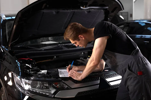 Meccanico auto professionale sta esaminando il motore sotto il cofano in officina di riparazione auto — Foto Stock