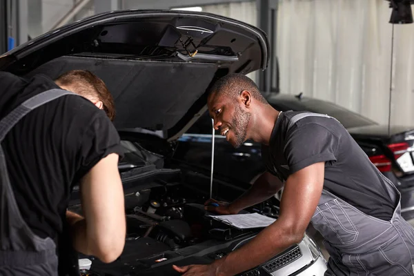 Dwóch różnych mechaników samochodowych współpracujących podczas badania wydajności silnika w warsztacie samochodowym — Zdjęcie stockowe