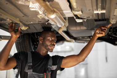 Erkek tamirci araba servisinde tek başına bir araç üzerinde çalışıyor.