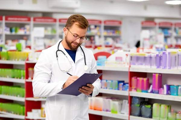 Angenehme männliche Apotheker schreiben auf Klemmbrett in der Apotheke — Stockfoto