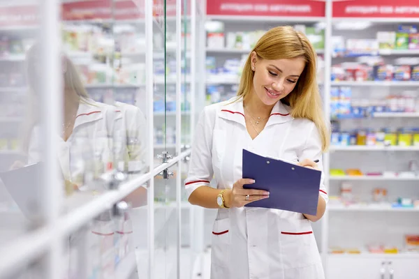 Angenehme Apothekerin schreibt an Klemmbrett in Apotheke, macht Notizen — Stockfoto