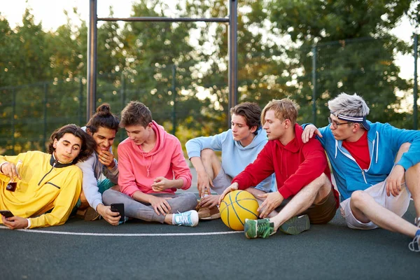 Μικροί φίλοι κάθονται στο γήπεδο του μπάσκετ, χαλαρώνοντας και κάνοντας διάλειμμα μετά το παιχνίδι — Φωτογραφία Αρχείου