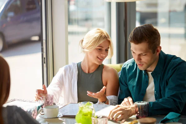 happy young couple enjoying while choosing an order from menu in modern cafe
