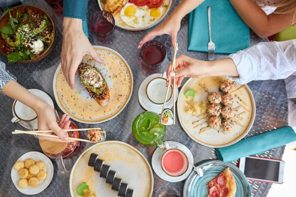 Gruppo di persone che tengono le bacchette e il campionamento cibo asiatico tavolo con vari tipi di cibo cinese — Foto Stock