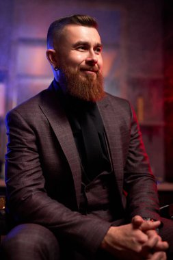 Genç, beyaz, yakışıklı, sakallı adam, karanlık dumanlı bir odada kanepede oturuyor.