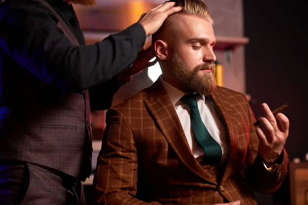Acconciatore maschile sicuro tagliare i capelli all'uomo elegante elegante seduto nel salone — Foto Stock