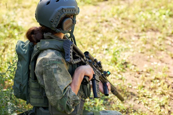 Vista lateral de una mujer irreconocible en ropa militar sentada en la hierba esperando al enemigo —  Fotos de Stock