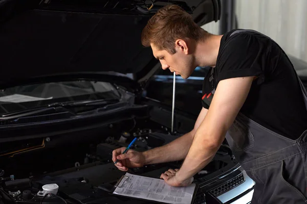 Professionele auto monteur onderzoekt motor onder de motorkap bij auto reparatiewerkplaats — Stockfoto