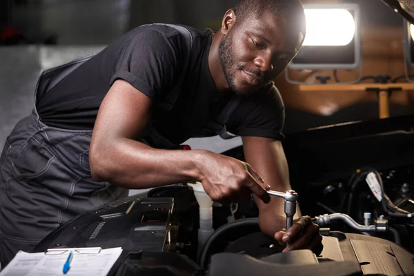 Professionele auto monteur onderzoekt motor onder de motorkap bij auto reparatiewerkplaats — Stockfoto