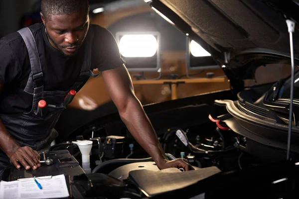 professional car mechanic is examining engine under the hood at auto repair shop