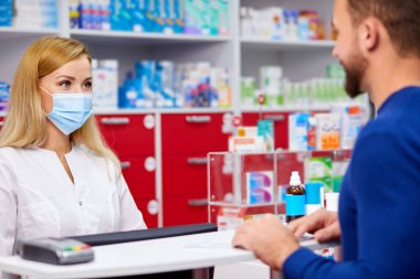 Genç eczacı, modern eczanedeki müşterilere ilaç veriyor.