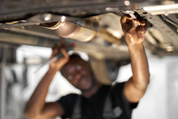 Joven africano mecánico de automóviles en uniforme de control de coches en el servicio de automóviles con vehículo levantado, se centran en las manos — Foto de Stock