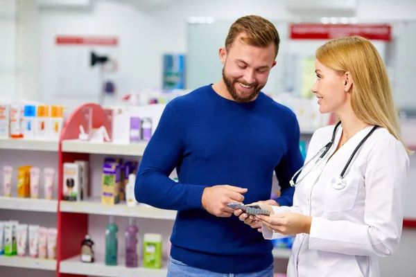 Farmacéutico amigable caucásico tiene una buena conversación con un cliente, ayuda a encontrar un medicamento — Foto de Stock