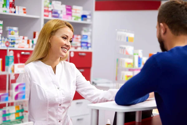 Farmacista caucasico amichevole ha una bella conversazione con un cliente, aiuta a trovare un farmaco — Foto Stock