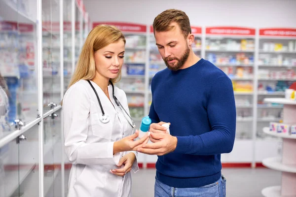 young female apothecary with drug and male customer at pharmacy