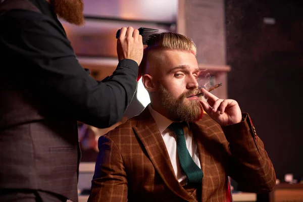 Macho elegante desfrutar de corte de cabelo no cabeleireiro, ele está fumando durante o processo de corte — Fotografia de Stock