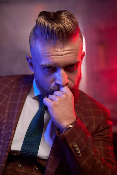 Young caucasian handsome bearded man sitting on couch in a dark smoky room — Stock Photo, Image