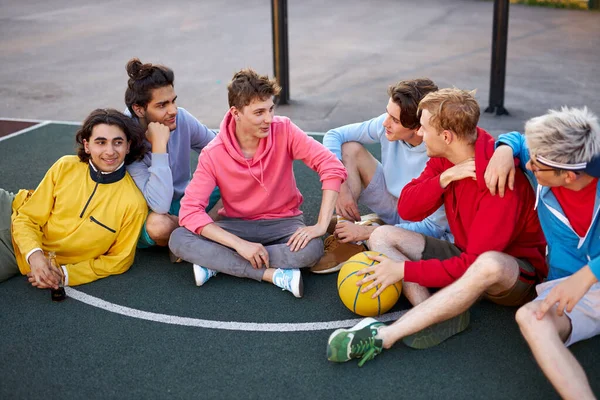 Μικροί φίλοι κάθονται στο γήπεδο του μπάσκετ, χαλαρώνοντας και κάνοντας διάλειμμα μετά το παιχνίδι — Φωτογραφία Αρχείου