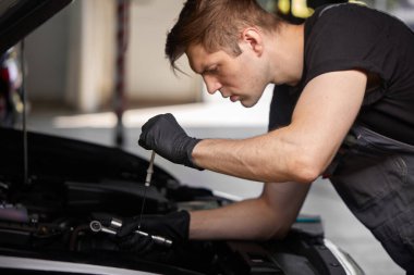 Beyaz tenli araba tamircisi, araba, motor ve karbüratörü kontrol ediyor.