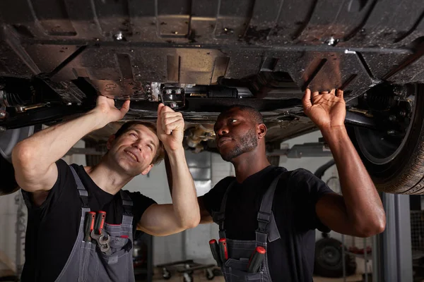 Dois inter-raciais mecânica diversificada verificando fundo do carro — Fotografia de Stock