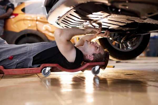 Boční pohled na koncentrované auto mechanik samec pracuje sám na podlaze — Stock fotografie