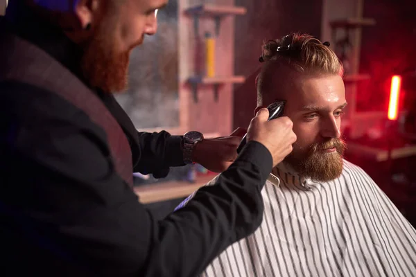 Acconciatore maschile sicuro tagliare i capelli all'uomo elegante elegante seduto nel salone — Foto Stock