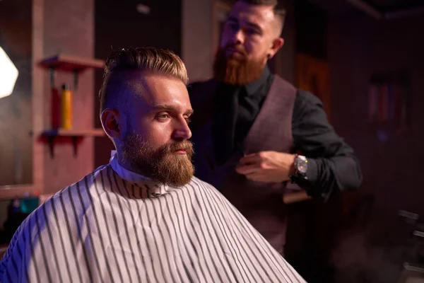 Acconciatore maschile sicuro tagliare i capelli all'uomo elegante elegante seduto nel salone — Foto Stock