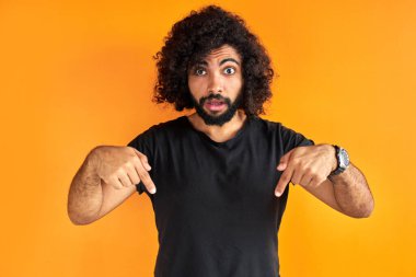 Siyah tişörtlü, şaşkın Arap adam parmağıyla aşağıya işaret ediyor.