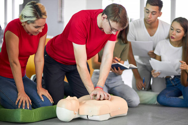 молодой мужчина практикующий искусственное дыхание на манекене в присутствии людей