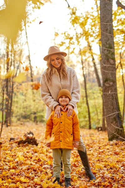 Wanita dengan anak laki-laki di kuning dan emas musim gugur hutan — Stok Foto