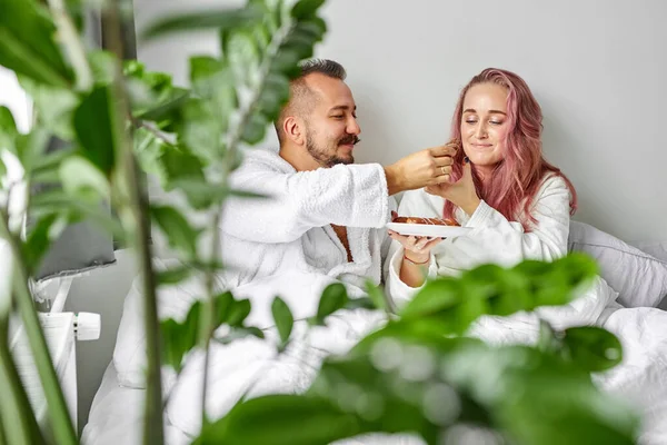 Casal tratar uns aos outros com eclairs na cama — Fotografia de Stock