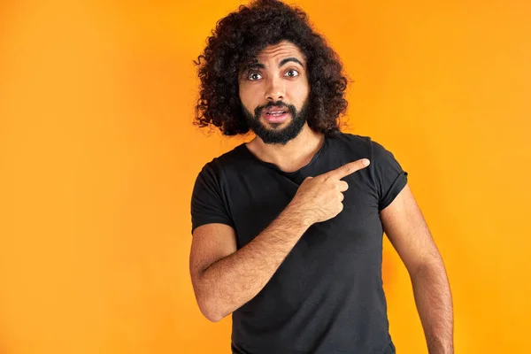 Surpreso árabe cara em preto casual t-shirt apontando dedo no lado — Fotografia de Stock