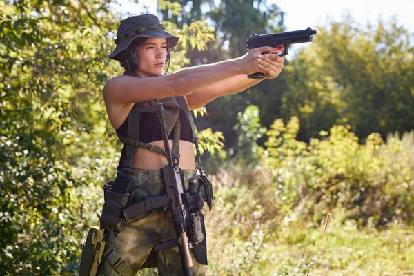 Hermosa hembra en camuflaje en sus brazos durante una guerra está apuntando a un objetivo o un enemigo, en el bosque —  Fotos de Stock