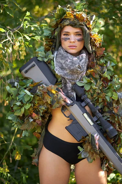 Valiente modelo militar mujer en la parte superior y pantalones cortos con rifle posando en el bosque — Foto de Stock
