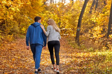 Çiftin arka görüntüsü güzel sonbahar ormanlarında kır yolunda koşmanın keyfini çıkarıyor.