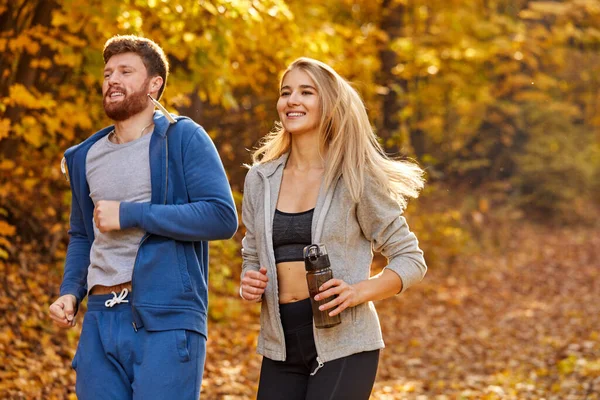 一对年轻夫妇在秋天的森林小径上奔跑 — 图库照片