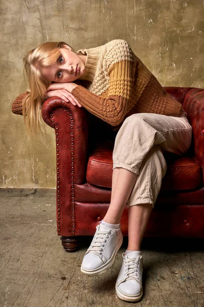 melancholy female is leaned on leather chair, couch in studio