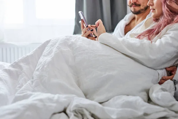 Hombre y mujer con smartphones en pijama en su cama — Foto de Stock