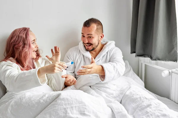 Χαρούμενο ζευγάρι ανακαλύπτει τα αποτελέσματα ενός τεστ εγκυμοσύνης στο σπίτι ξαπλωμένο στο κρεβάτι — Φωτογραφία Αρχείου