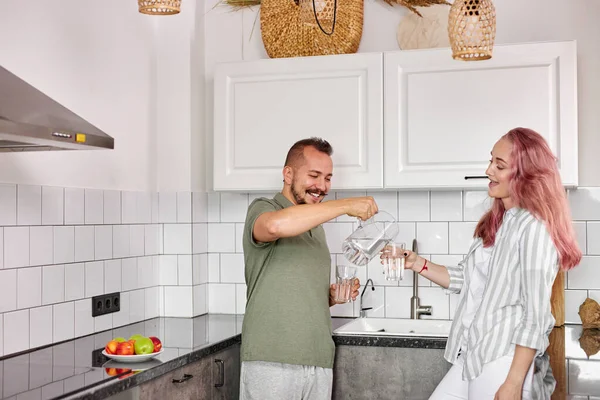 Hombre vertiendo agua en taza a esposa en la cocina — Foto de Stock