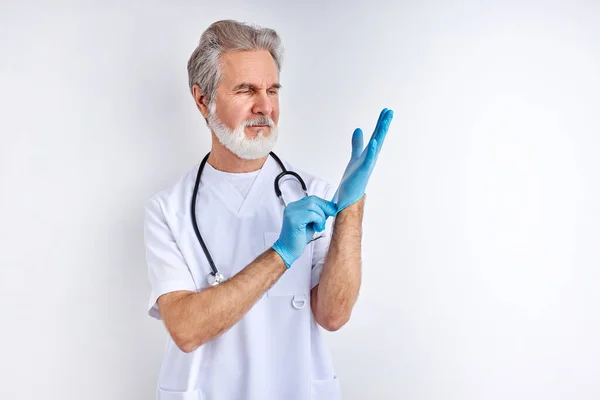 Médico varón maduro está usando guantes preparándose para el trabajo — Foto de Stock