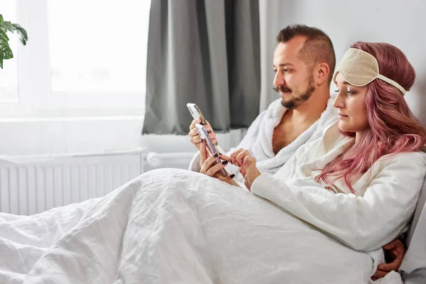Pareja relajándose en la cama usando teléfonos celulares por la mañana — Foto de Stock