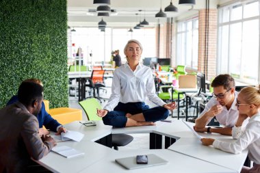Kafkasyalı iş kadını, gözleri kapalı işteki ofis masasında meditasyon yapıyor.