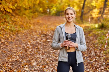 Ormanın doğasında duran bir şişe suyla mutlu bir koşucu.