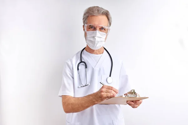 Anciano doctor hombre toma notas usando estetoscopio aislado en blanco — Foto de Stock